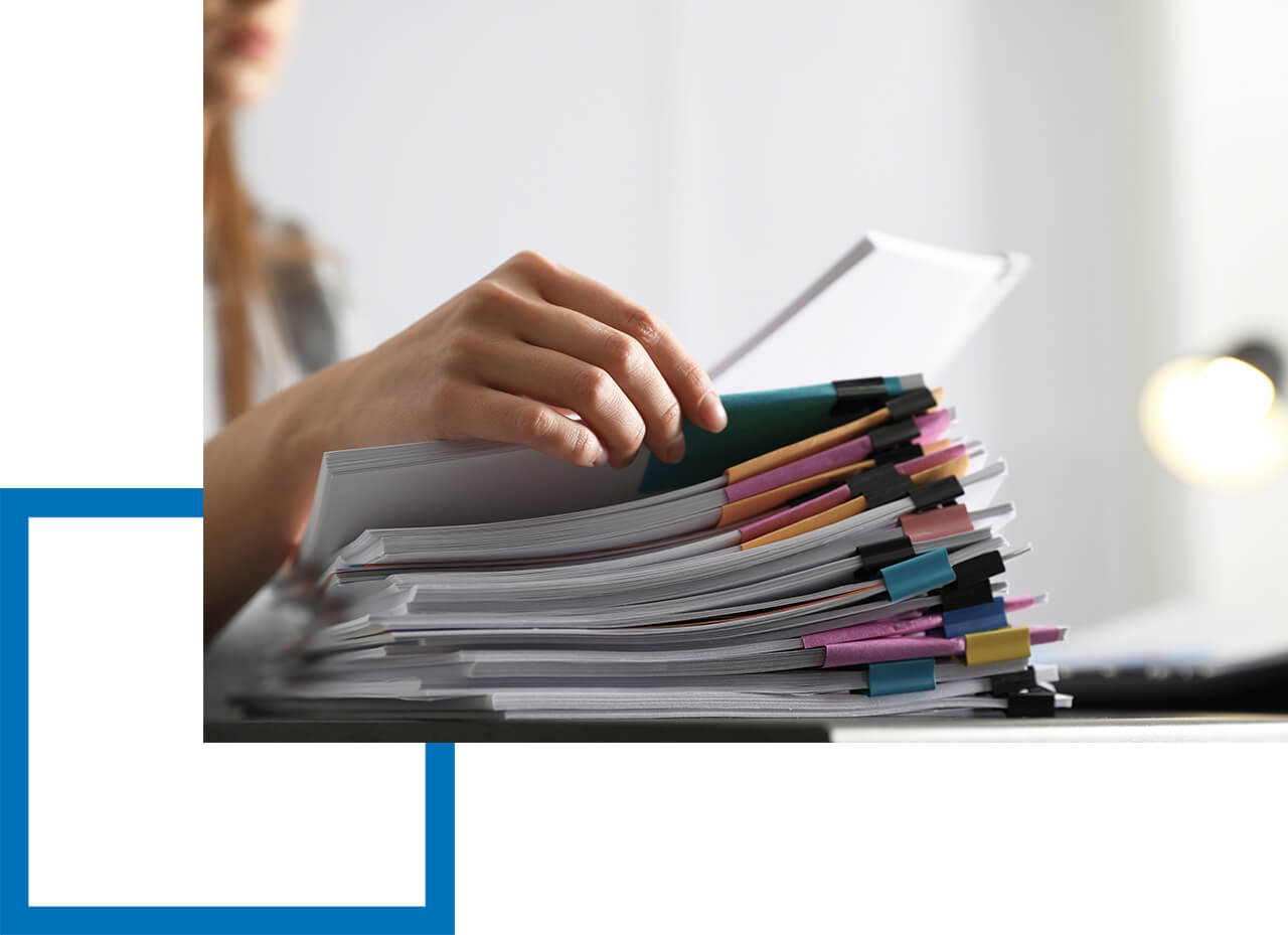 Deshalb ist die Berufshaftpflicht wichtig. Hand blättert durch sortierte Papierstapel mit farbigen Klemmen auf Schreibtisch.
