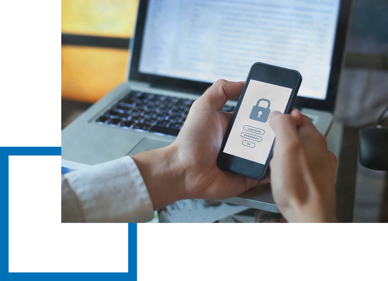 Eine Haftpflicht für externe Datenschutzbeauftragte ist wichtig! Person hält Smartphone mit Login-Maske vor geöffnetem Laptop in der Hand.
