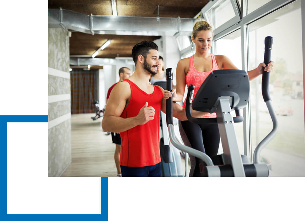 Berufshaftpflicht besonders bei Fitnesstrainer wichtig. Im Sportstudio erklärt der Trainer das trainieren an einem Crosstrainingsgerät
