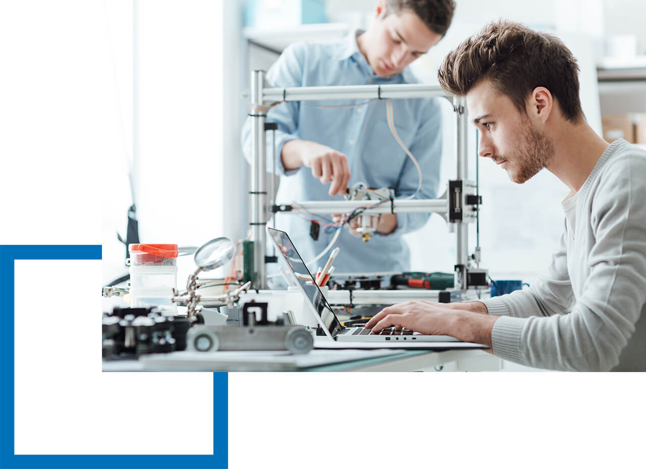 Die richtige Versicherung wählen! Zwei Männer arbeiten konzentriert an Technikprojekten mit Laptop und 3D-Drucker.