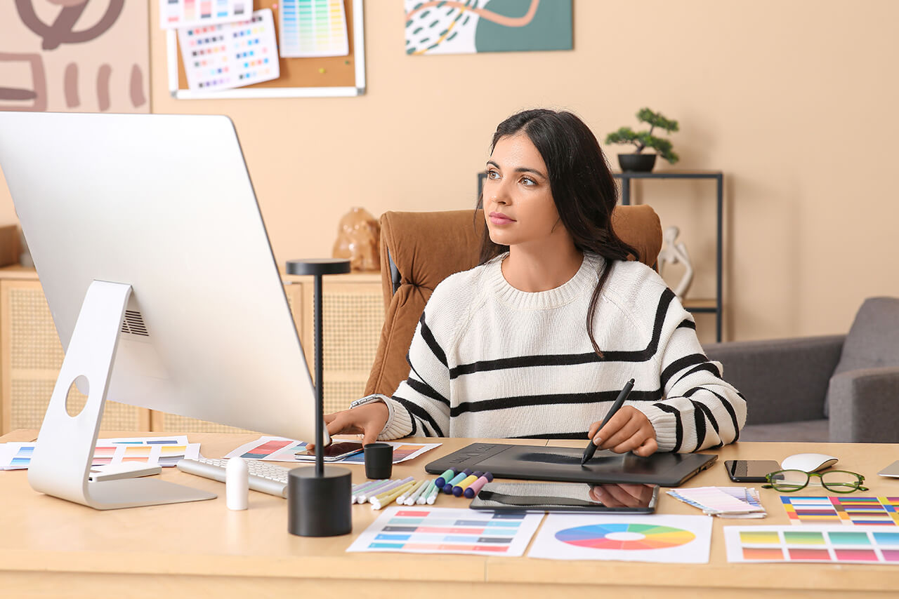 Frau arbeitet konzentriert mit Grafiktablet an Farbentwürfen am Schreibtisch.