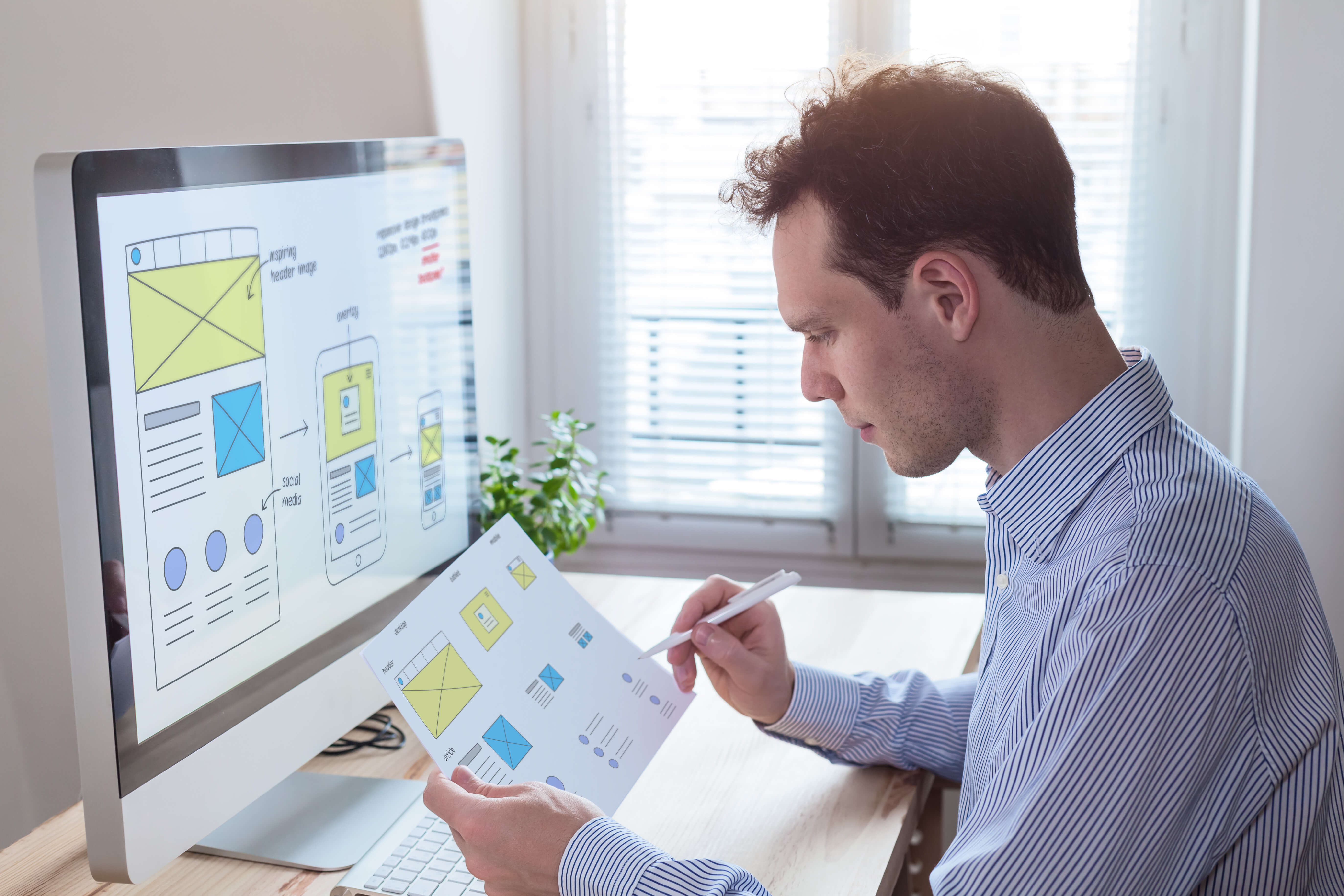 Webdesigner prüft eine Websitestruktur auf Papier und am Monitor.