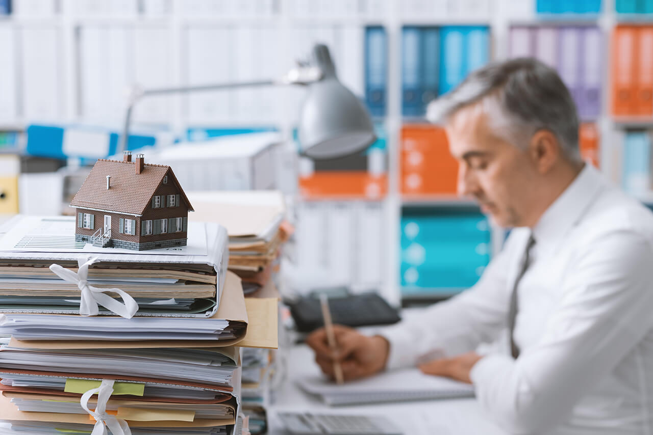 Hausverwalter am Schreibtisch mit vielen Akten und Unterlagen - bei einem Fehler hilft die Berufshaftpflichtversicherung