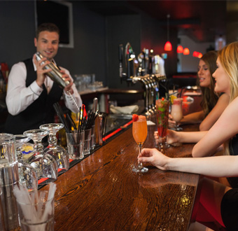 Mann in Bar mixt Cocktails für Frauen