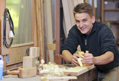 Mann in einer Tischlerei bearbeitet gerade eine Holzplatte