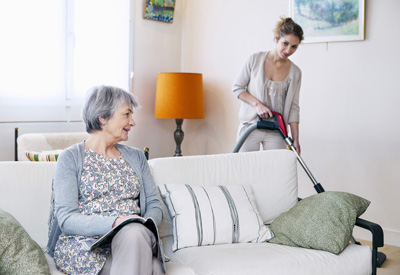 Putzfrau bei Seniorin zu Hause am Staubsaugen